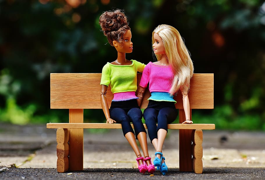 two Barbie dolls sitting on brown wooden bench miniature, girl