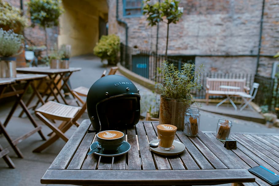 espresso filled cups near the motorcycle helme, black half-face helmet on brown wooden table