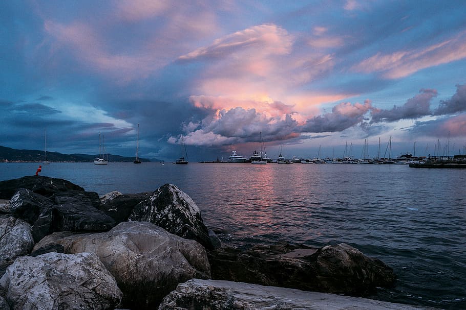 brown rocks and body of water at daytime, group of boats on body of water under gray and white clouds HD wallpaper