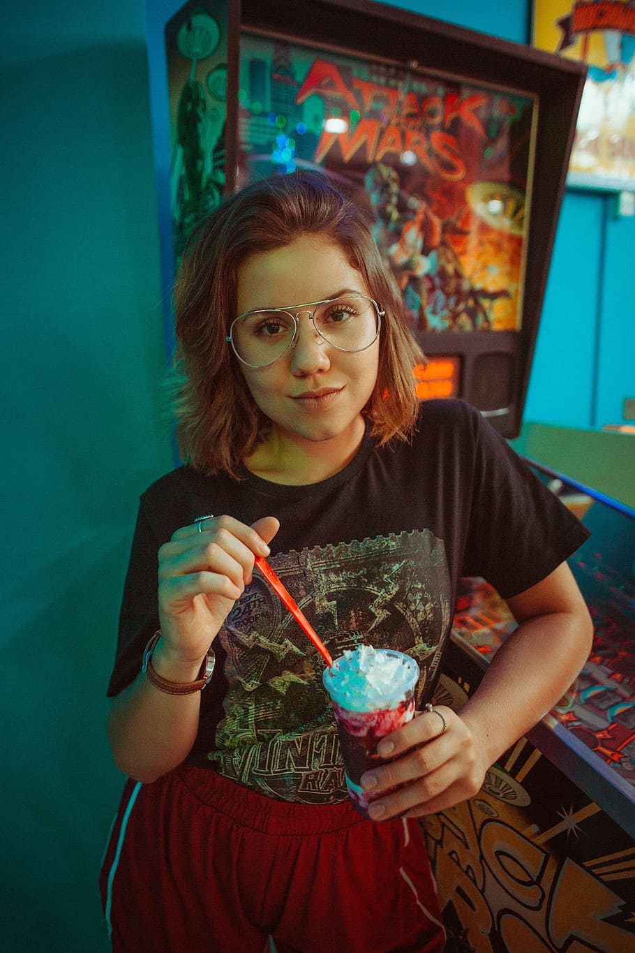 selective focus photography of girl eating strawberry frappe, woman standing near pinball machine HD wallpaper