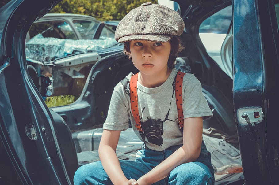 boy sitting inside wrecked black vehicle body shell during daytime, HD wallpaper