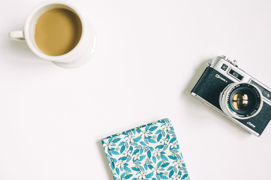 black and grey SLR camera, floral notebook, and white ceramic mug, black and gray camera beside white coffee cup HD wallpaper