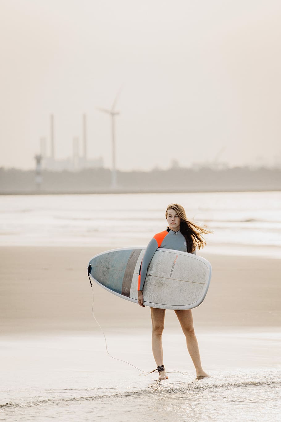 woman standing on seashore carrying surfboard, woman holding white and blue surfboard standing near shore HD wallpaper