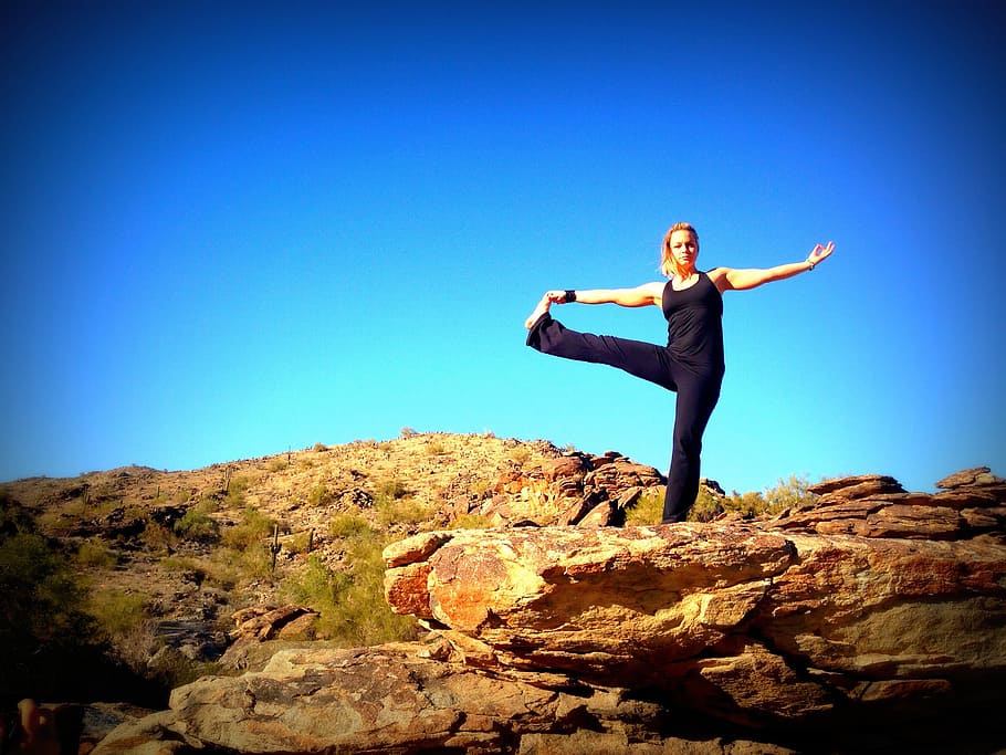 woman wearing black tank top and pants standing on rock formation under clear blue sky, HD wallpaper