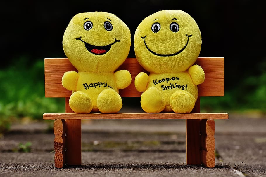 two yellow emoticon plush toys sitting on brown wooden bench