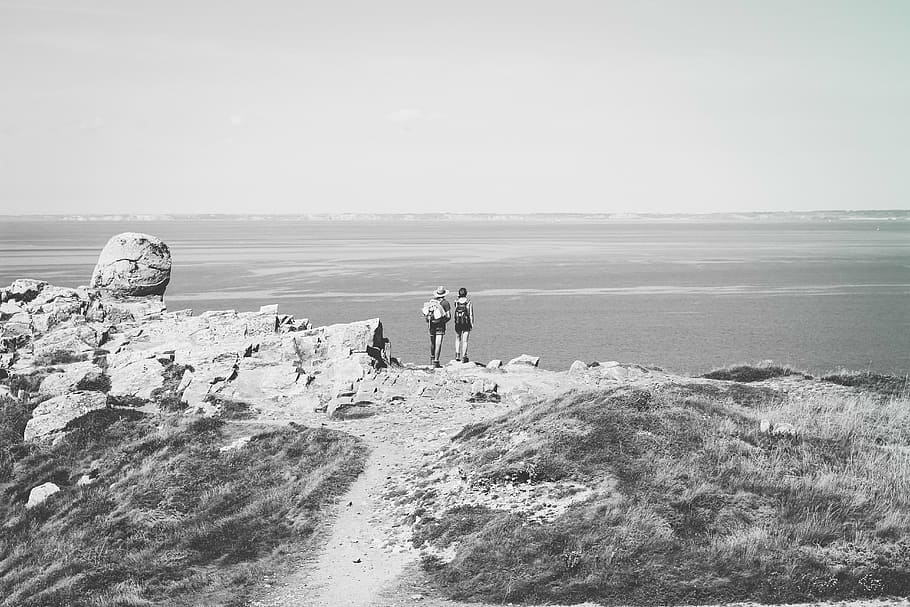 grayscale photo of two person standing towards sea, people, beside