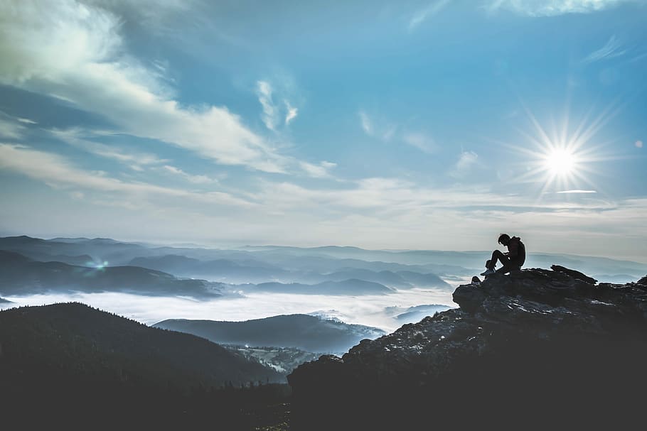 man sitting on rock during daytime, silhouette photography of man sitting on rock with view of mountains during daytime HD wallpaper