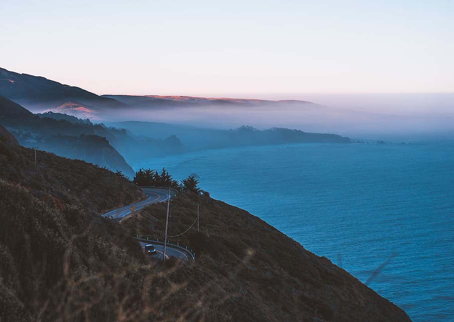 body of water and road hills surrounded by fogs, curvy road near sea HD wallpaper