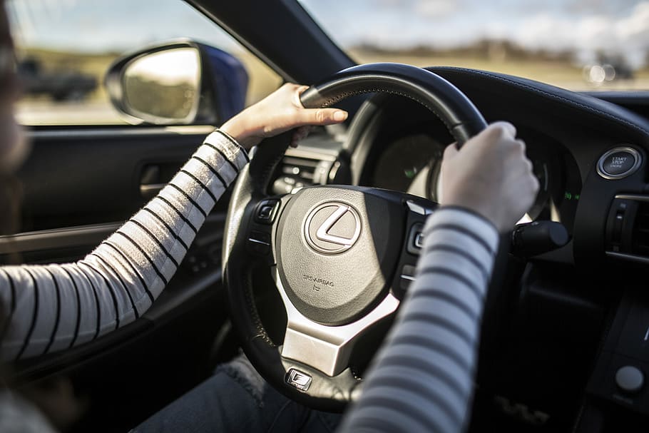 person driving car during daytime, person holding on black Lexus car steering wheel
