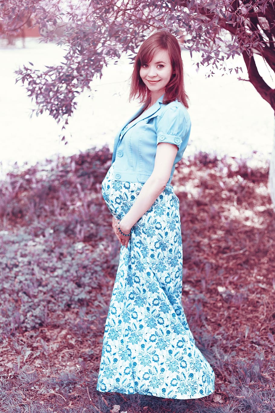pregnant woman wearing blue floral dress standing near tree during daytime
