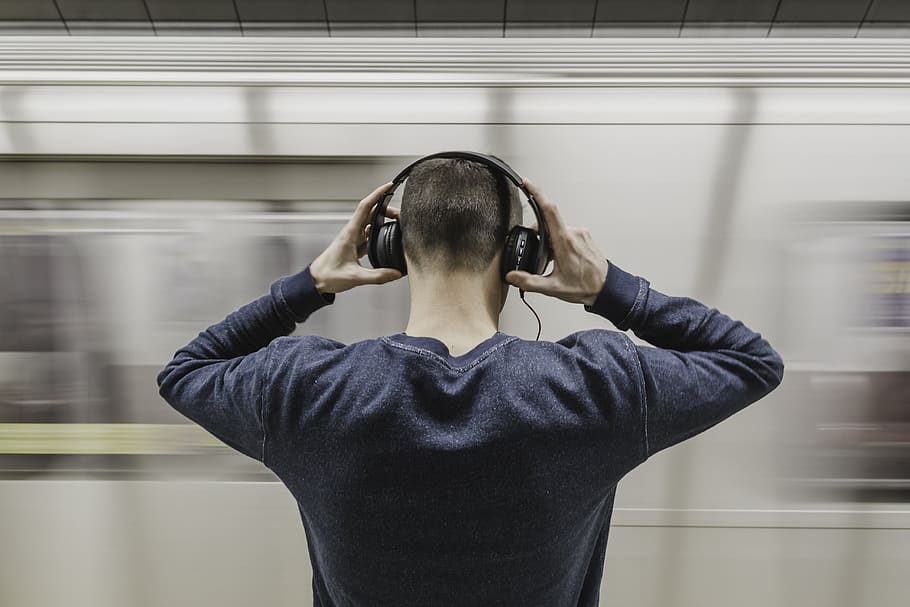 man wearing gray sweatshirt holding headphones in front on train station, HD wallpaper