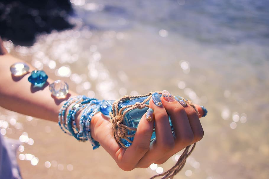 selective focus photography of person holding blue glass accessory wrap with gray thread near body of water during daytime