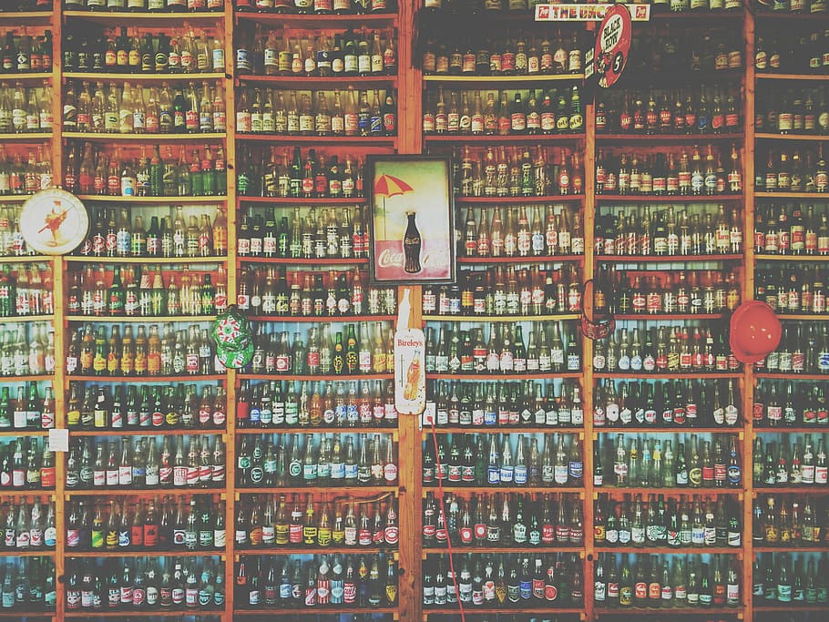 coke bottle poster with brown wooden frame on brown rack, photo of assorted-brand bottle collection on shelves