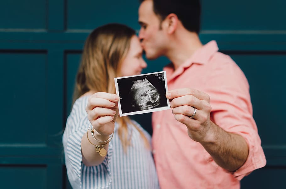 man kissing woman's forehead white holding ultrasound photo, man kissing her wife on the forehead showing ultrasound of their baby