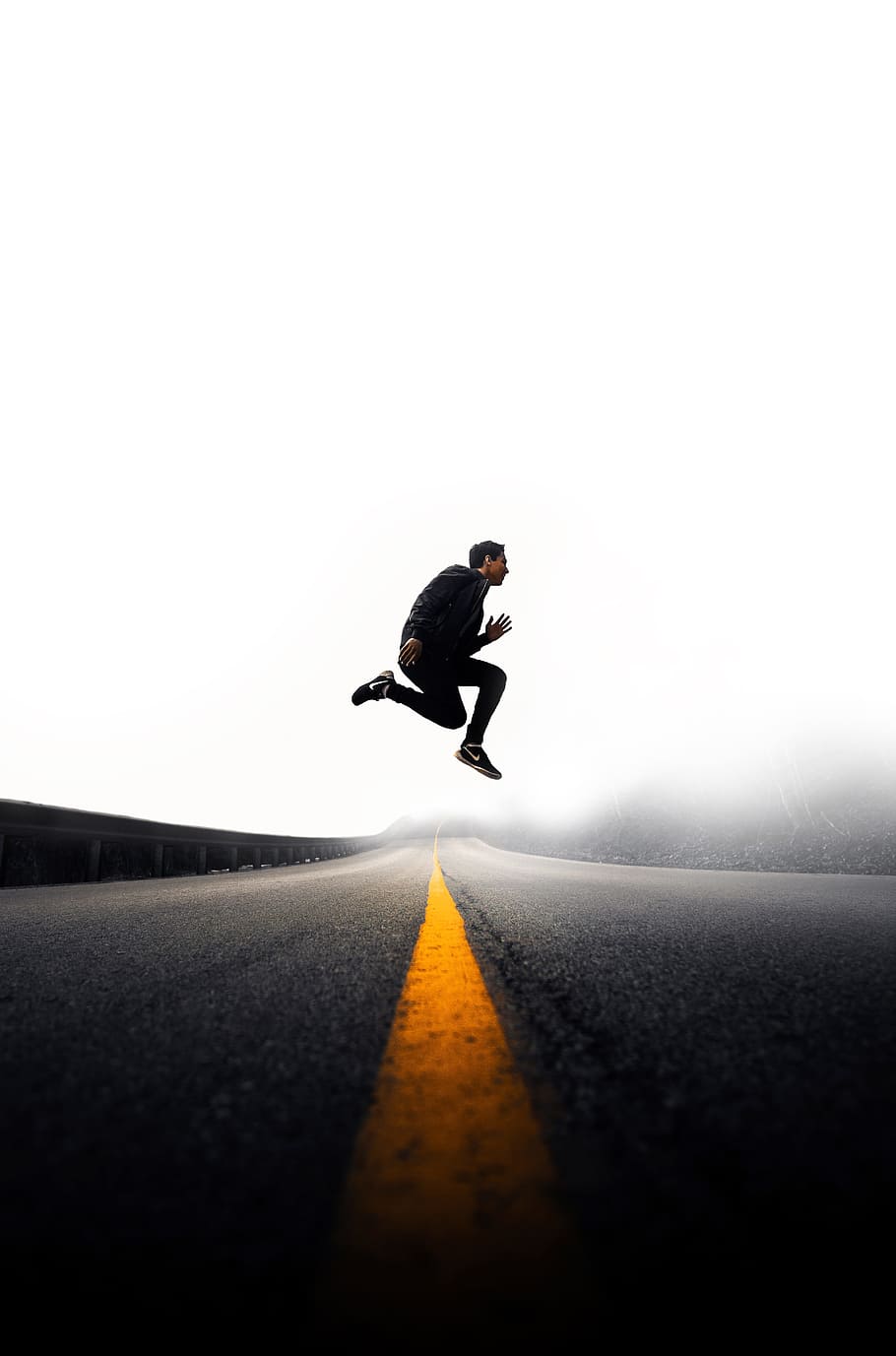 man jumping above gray and yellow concrete road at daytime, man jumping on road with background of fogs HD wallpaper
