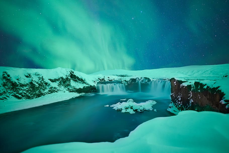 waterfalls covered with snow, body of water in between snow covered ground under Aurora at night time