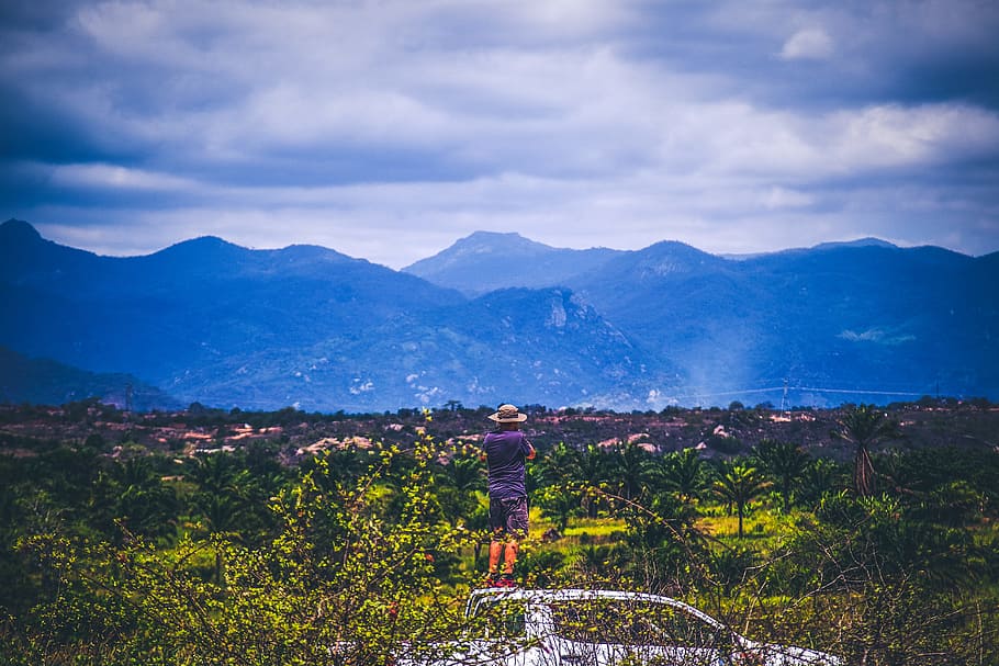 Person Wearing Sun Hat Looking At Mountains Under Cloudy Sky HD wallpaper