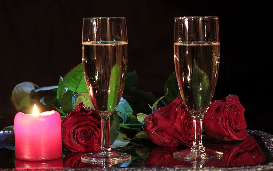 two clear champagne flutes beside the red rose flowers on clear glass surface