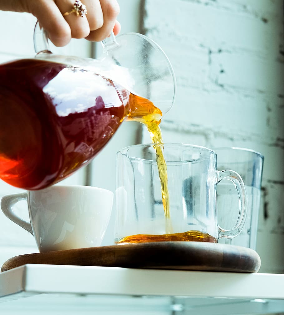 person pouring tea on cup, woman pouring tea on clear glass mug during daytime HD wallpaper