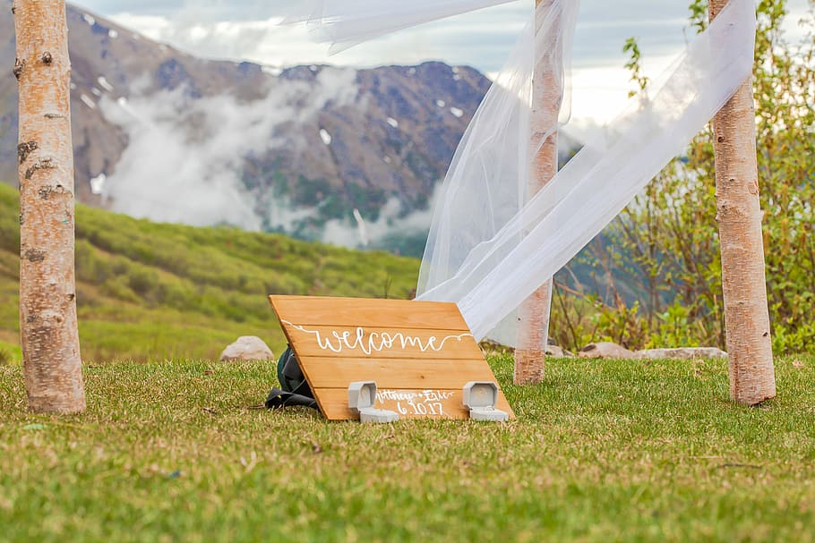 welcome signage on grass field, selective focus photography wooden welcome decor on green grass near mountain HD wallpaper