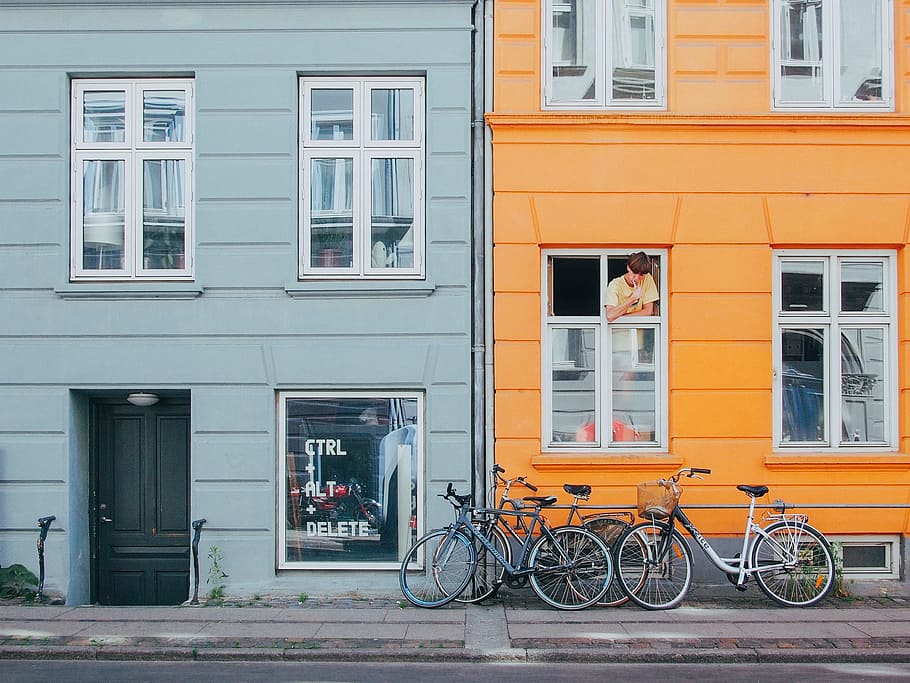 person on window looking at bicycles during daytime, blue and yellow high rise building with bicycles on front and boy on window at daytime HD wallpaper