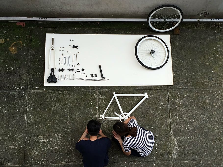 man and woman crouching near bicycle parts, assembling a bicycle HD wallpaper