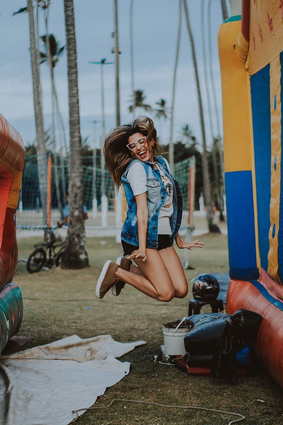woman wearing grey acid-washed sleeveless button-up jacket jumping near blue and yellow inflatable castle during daytime, HD wallpaper