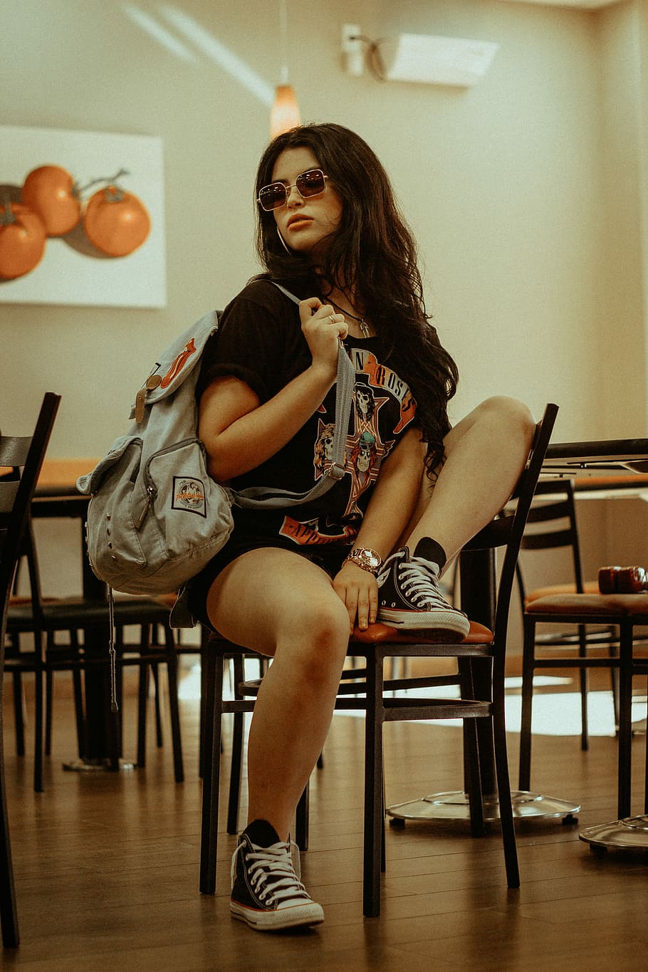 woman sitting on brown wooden chair, portrait, sunglasses, backpack