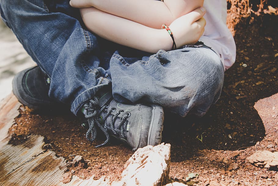 A child in jeans, boots, and a bracelet sits on dirt, crossing their legs, person sitting on soil while carrying baby during daytime HD wallpaper
