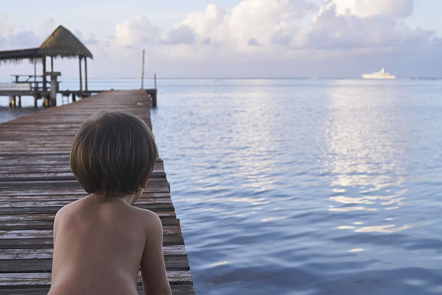 boy kneeling on wooden dock, boy sitting on dock facing body of water HD wallpaper