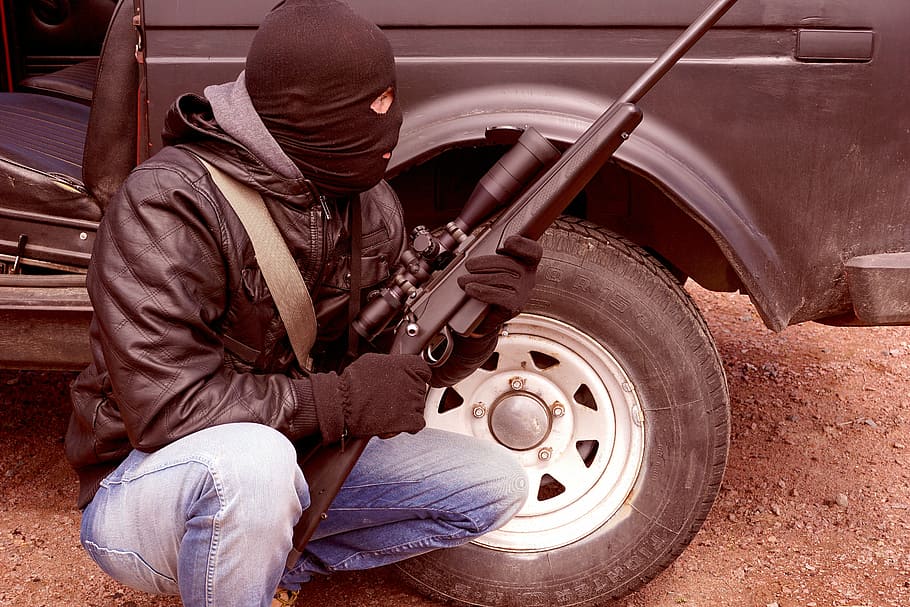 man sitting beside car while holding a rifle, criminal, terrorist