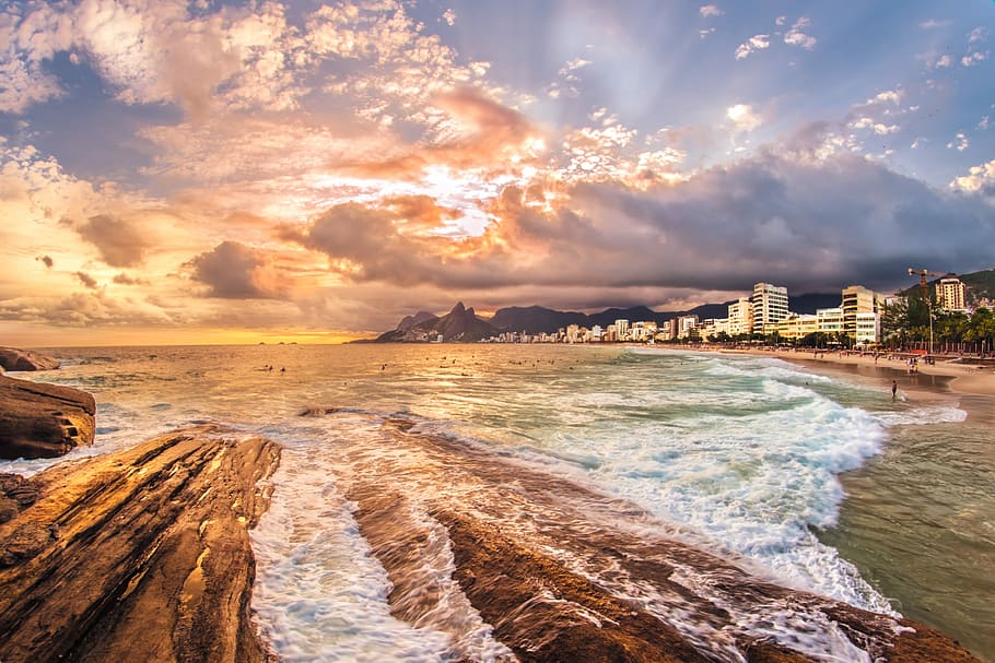 seashore near city under cloudy skies, beach waving under blue sky HD wallpaper