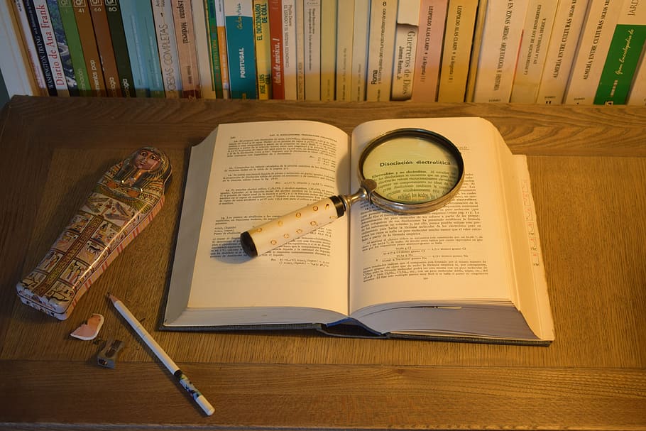 book with magnifying glass, pencil and Egyptian sarcophagus figurie