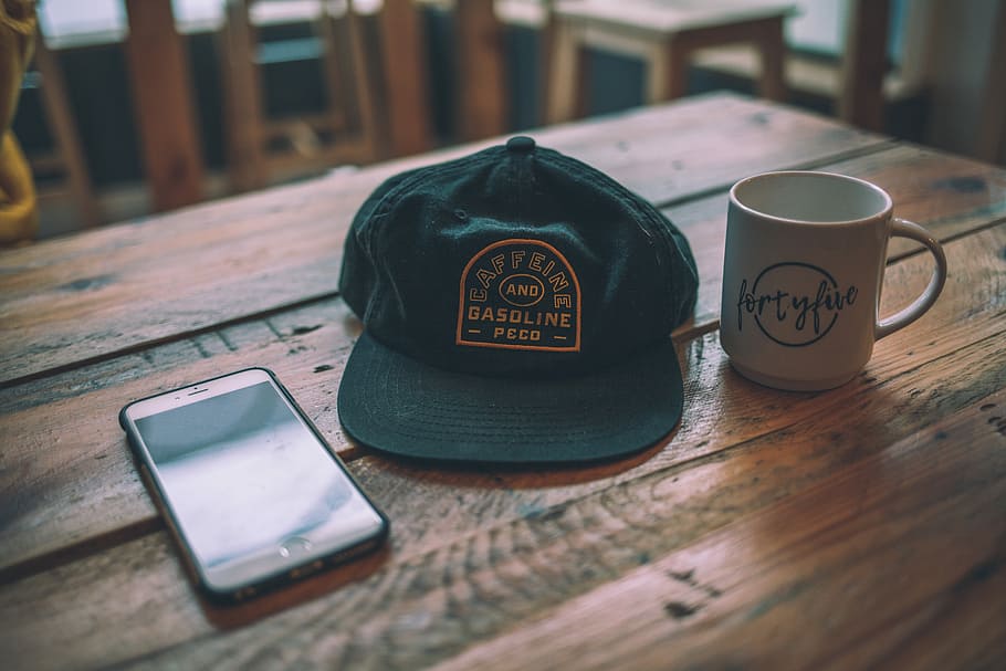 black cap beside mug, white ceramic mug, table, wood, hat, reflection HD wallpaper