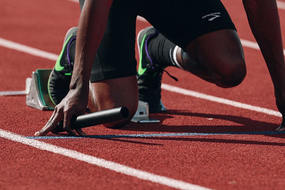 person wearing black-and-green Nike running shoes kneeling on starting line