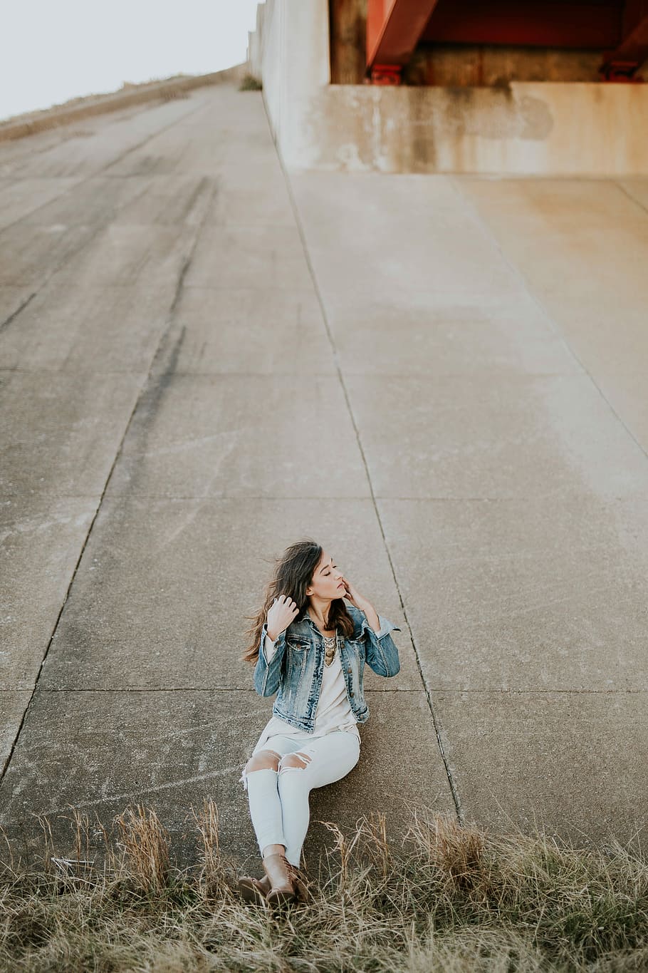 woman in blue washed denim jacket, white shirt, and distressed blue jeans leaning in concrete wall, HD wallpaper