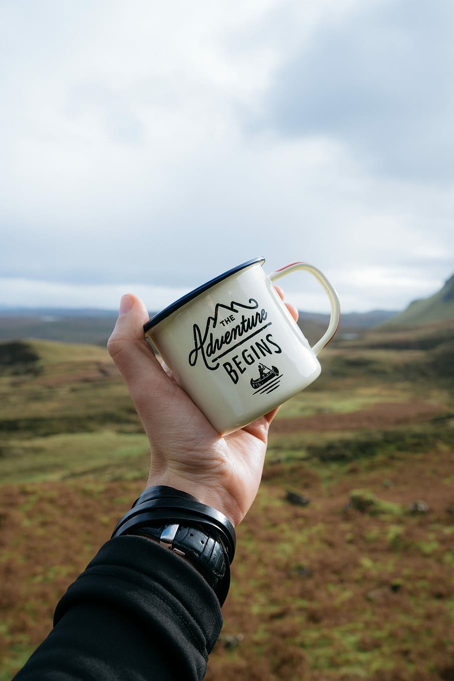 person holding beige and black The Adventure Begins-printed mug during daytime, person holding beige quote-printed mug with mountains background HD wallpaper