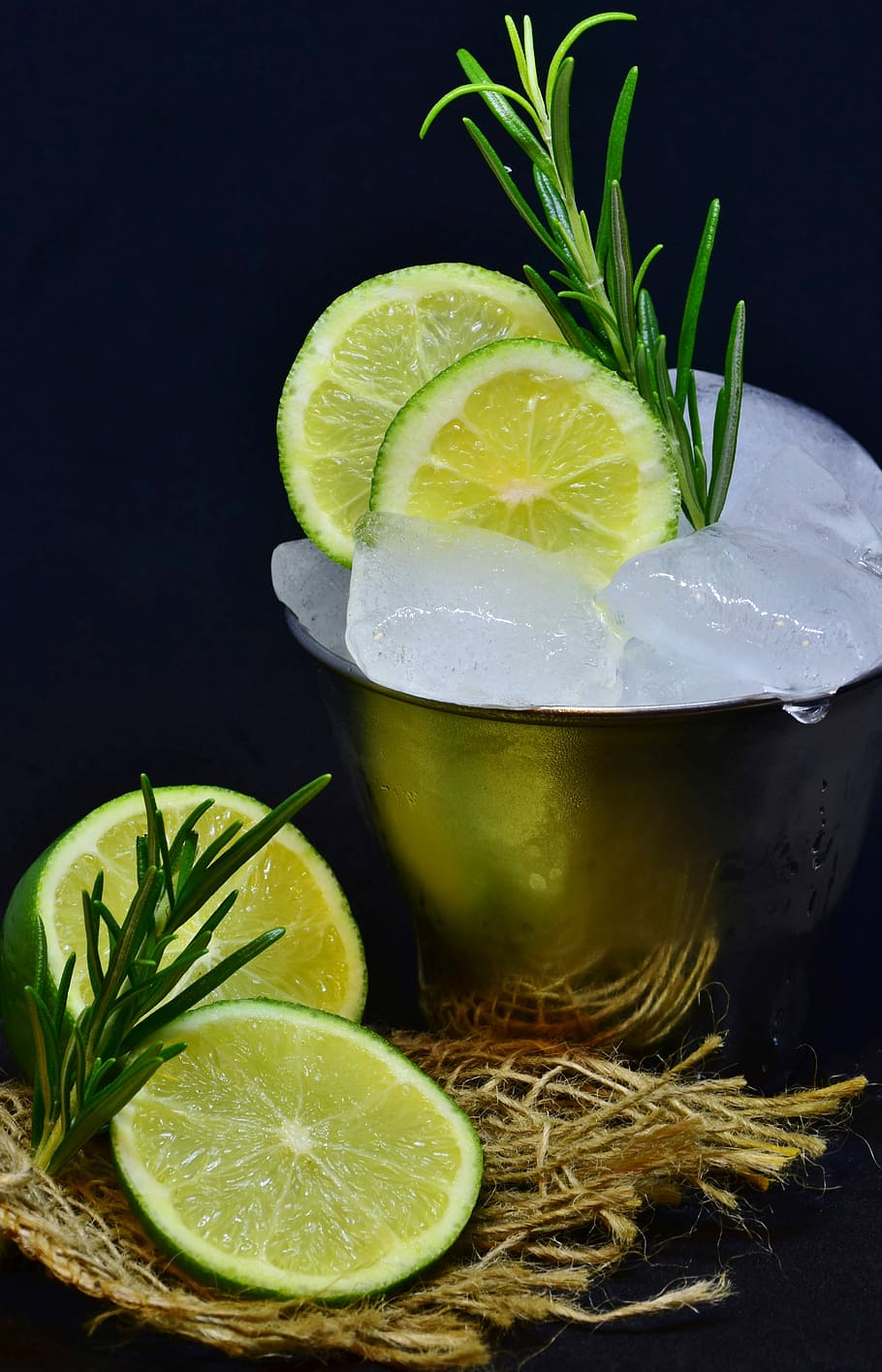 two sliced lemons in gray steel cup with ice and green rosemary