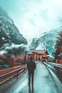 man standing on concrete pavement facing wooden house, man standing on road facing house and mountains HD wallpaper