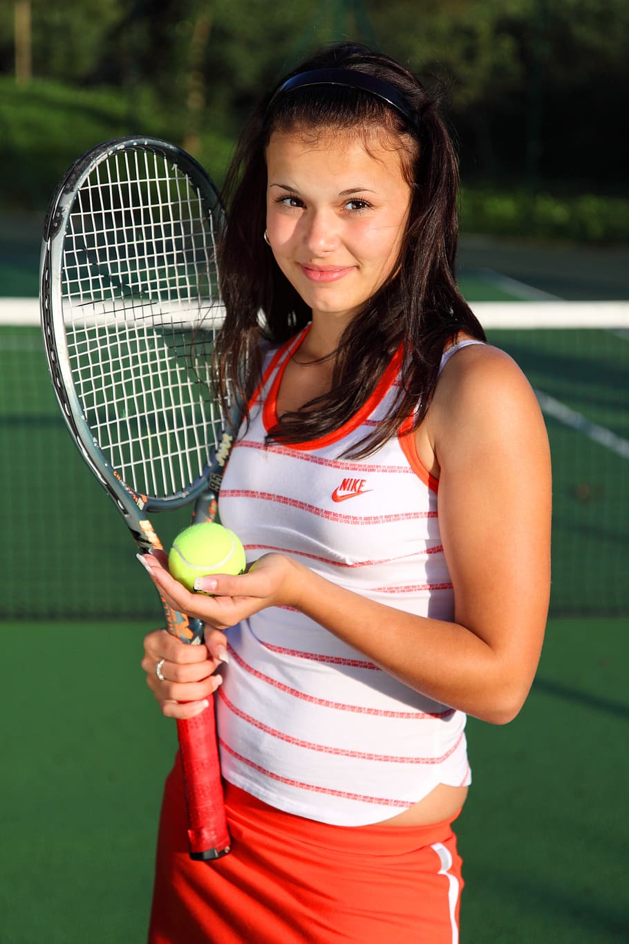woman wearing white and orange Nike tank top and holding tennis racket