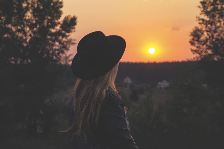 woman wearing black hat staring at sunset, woman standing looking at the sunset