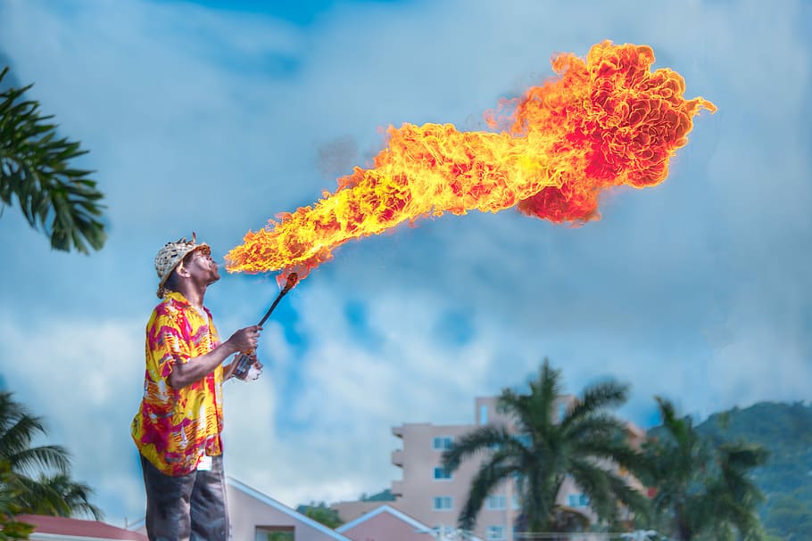 man blowing gas to make fire, man in yellow and red top blowing fire under white clouds and blue sky during daytime, HD wallpaper