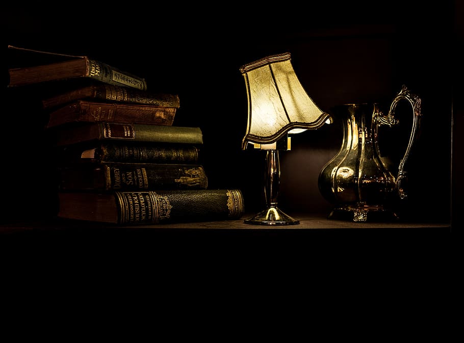 turned on desk lamp beside pile of books, table lamp beside a pitcher and books on table