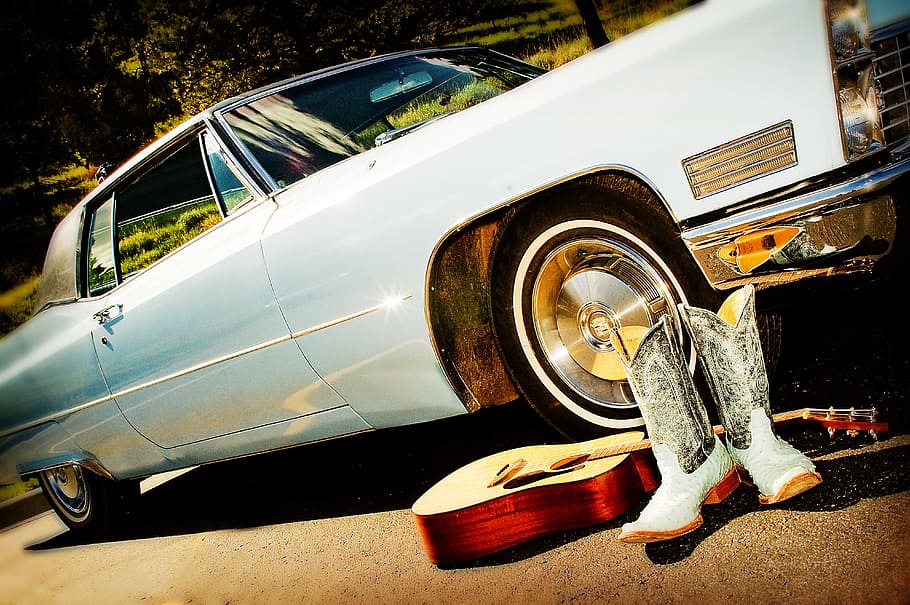 pair of white-and-gray cowboy boots and guitar beside vintage white coupe