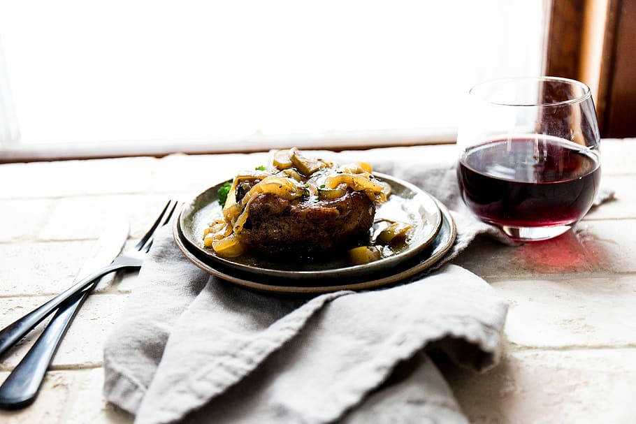 cooked food on ceramic plate beside wine glass and fork and cutlery knife on top of table, cooked meat on plate beside glass of wine HD wallpaper
