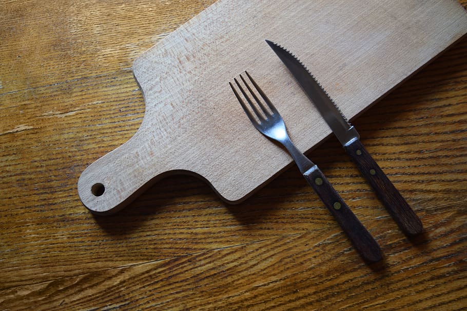 stainless steel fork beside knife on top of wooden chopping board