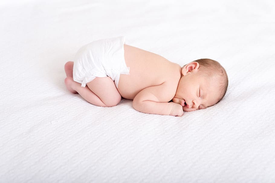 baby in white disposable diaper sleeping on white cushion, newborn