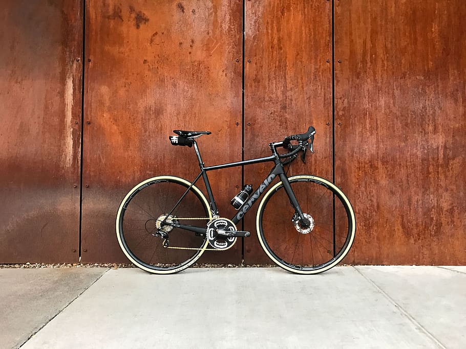 black road bike parked beside brown wooden wall, black road bike on gray pavement
