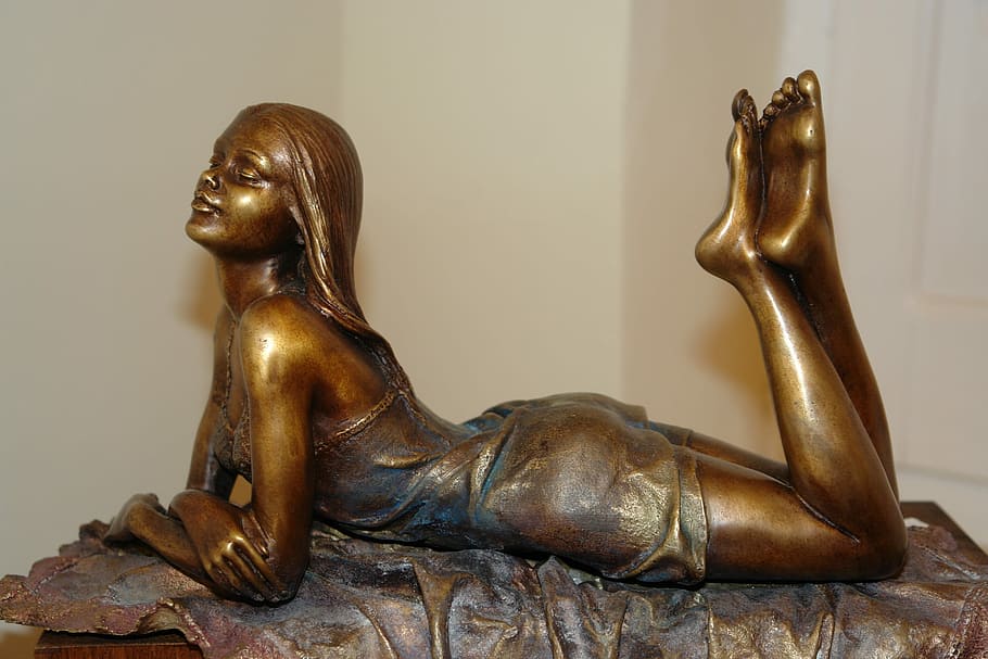 woman in sleeveless mini dress laying on chair brass metal figurine