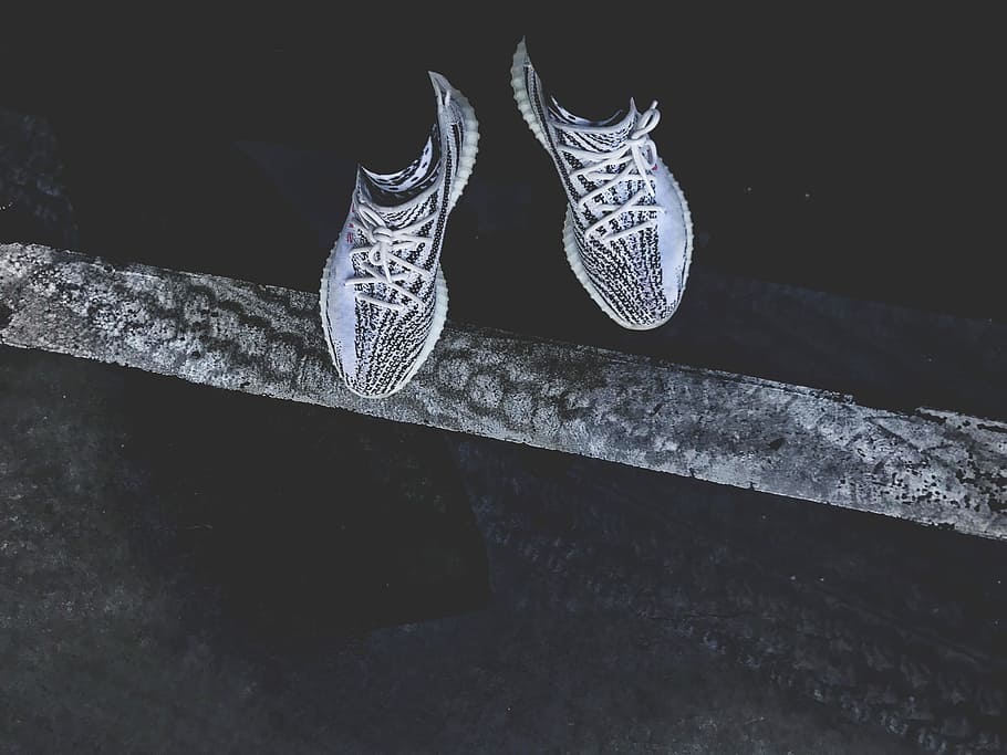 pair of gray-and-black adidas Yeezy Boost 350's, person standing wearing pair of white-and-black Adidas mid-top sneakers